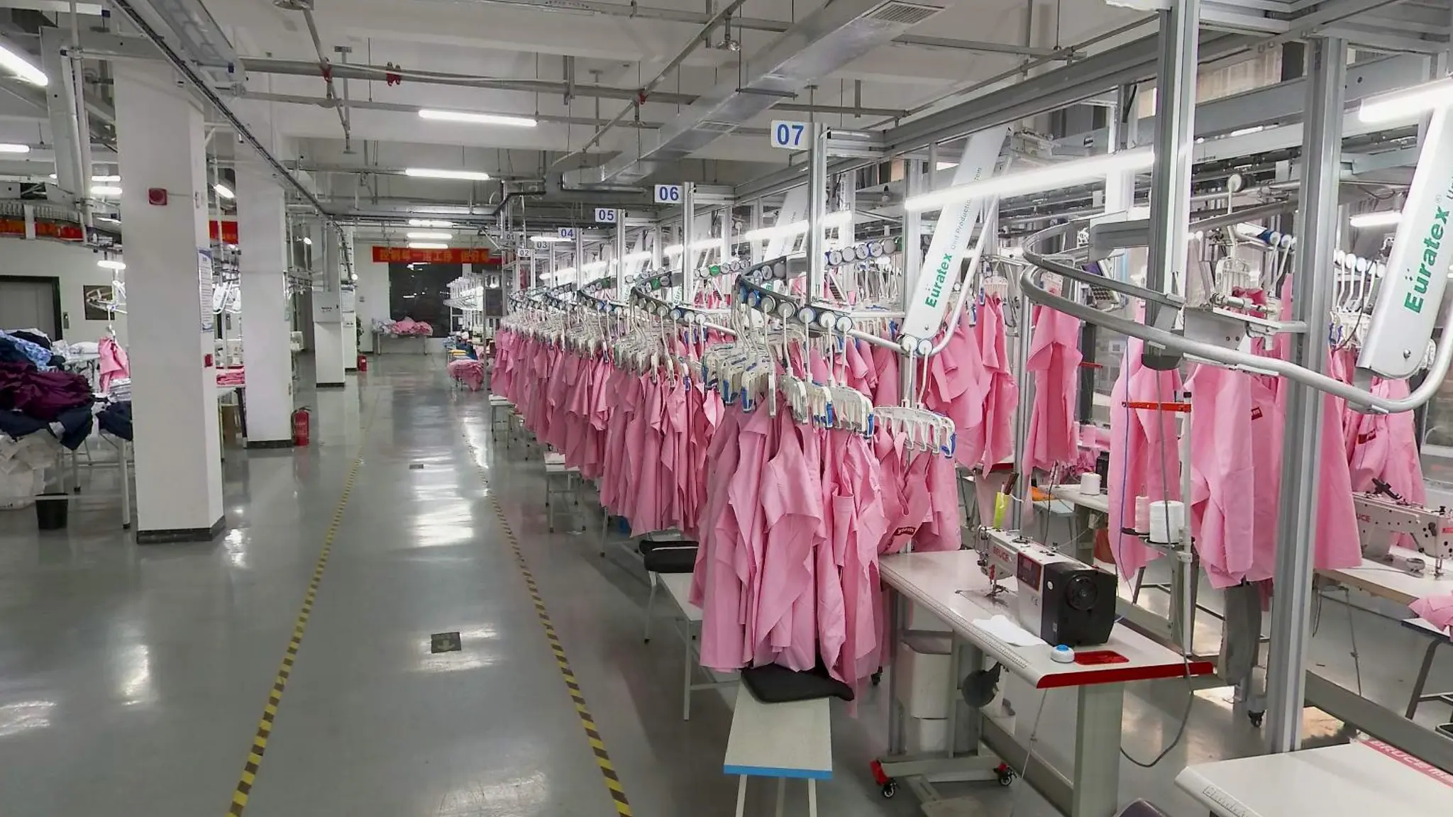 Medical uniform garments beside sewing workstations on a production floor in Henan, China