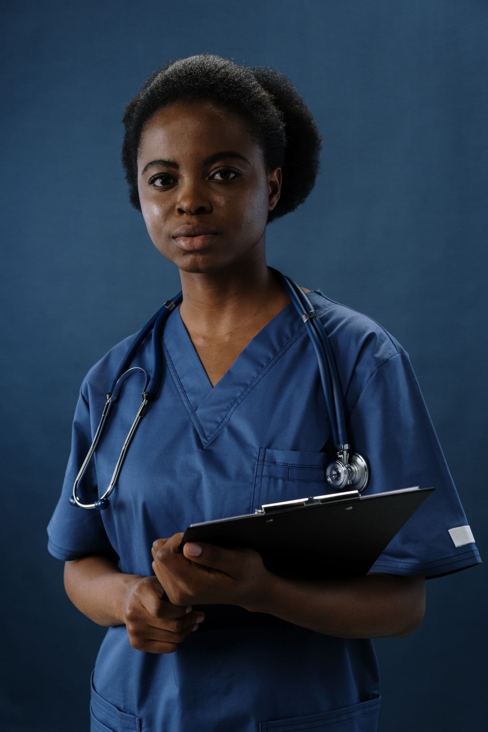 Model wearing navy scrubs and holding a clipboard against a navy background